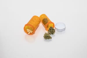 image of two pill bottles on a white table, one bottle is spilling out prescription pills and the other is spilling cannabis