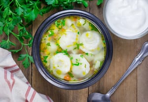 image of a bowl of chicken and dumpling soup with parsley and a spoon next to it