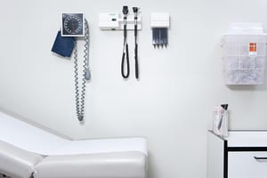 photo of an empty doctor's office patient room. it's all white and has a bench to lay on and equipment