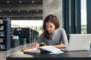 image of student studying in a library with books and her computer