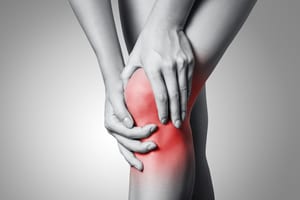black and white image of a woman's knees, she's holding her knee with her hands, her knee has a red dot over it to show joint pain