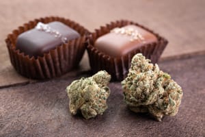 photo of two chocolates in wrappers behind 2 nugs of marijuana, showing that chocolate edibles are a great weed gift idea