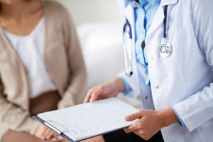 photo of a doctor with a clipboard talking to a female patient, showing that you have to talk to a doctor before you can get a medical marijuana card michigan