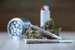 image of a lighter, grinder, marijuana buds, and joints all sitting on a table, one joint is resting on a marijuana bud
