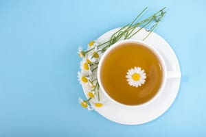 image of a cup of chamomile tea with a chamomile flower in the cup and flowers with stems on the plate next to the cup