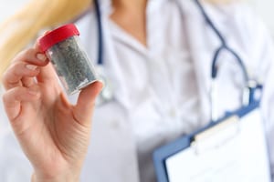 image of a doctor in a lab coat holding up a bottle with marijuana buds in it, image is used to represent medical marijuana