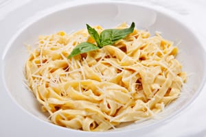 photo of pasta noodles in a white bowl with parmesan and basil on the noodles