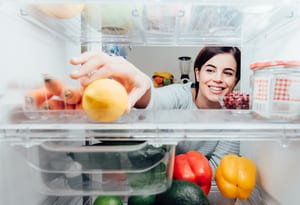 image of a woman reaching into her refrigerator to get a vegetable on the shelf