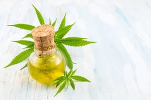 image of a glass container of cannabis oil sitting on a table with marijuana leaves behind and in front of it