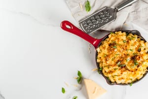 image of mac and cheese in a pan with a cheese grater and cheese partially out of frame