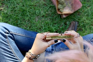 image of a woman sitting with crossed legs in the grass rolling a joint