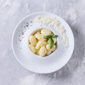 photo of a bowl of parmesan gnocchi with ground pepper and parmesan shavings around the rim of the bowl