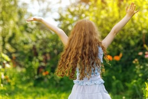 a red headed child with her back to the camera has her arms in the air and she's taking in the beauty of the nature around her
